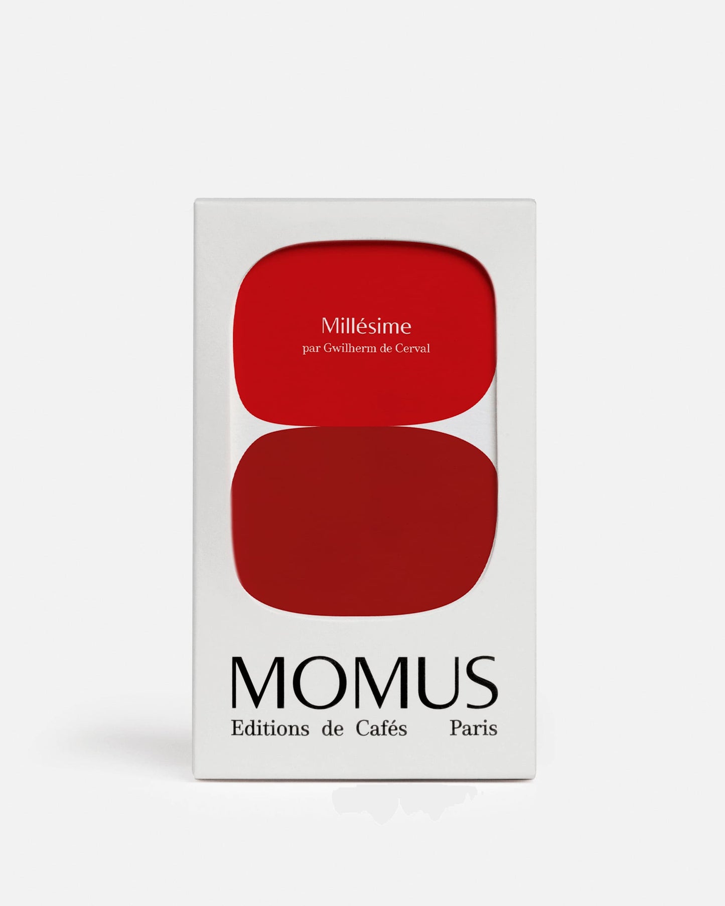 Gros plan du packaging blanc de l'édition spéciale Café Millésime de Momus. La boîte présente deux formes rouges superposées et arrondies. Le texte sur le rouge supérieur indique "Millésime par Gwilherm de Cerval". Le bas de la boîte porte la marque MOMUS Éditions de Cafés Paris. Café biodynamie vieilli.