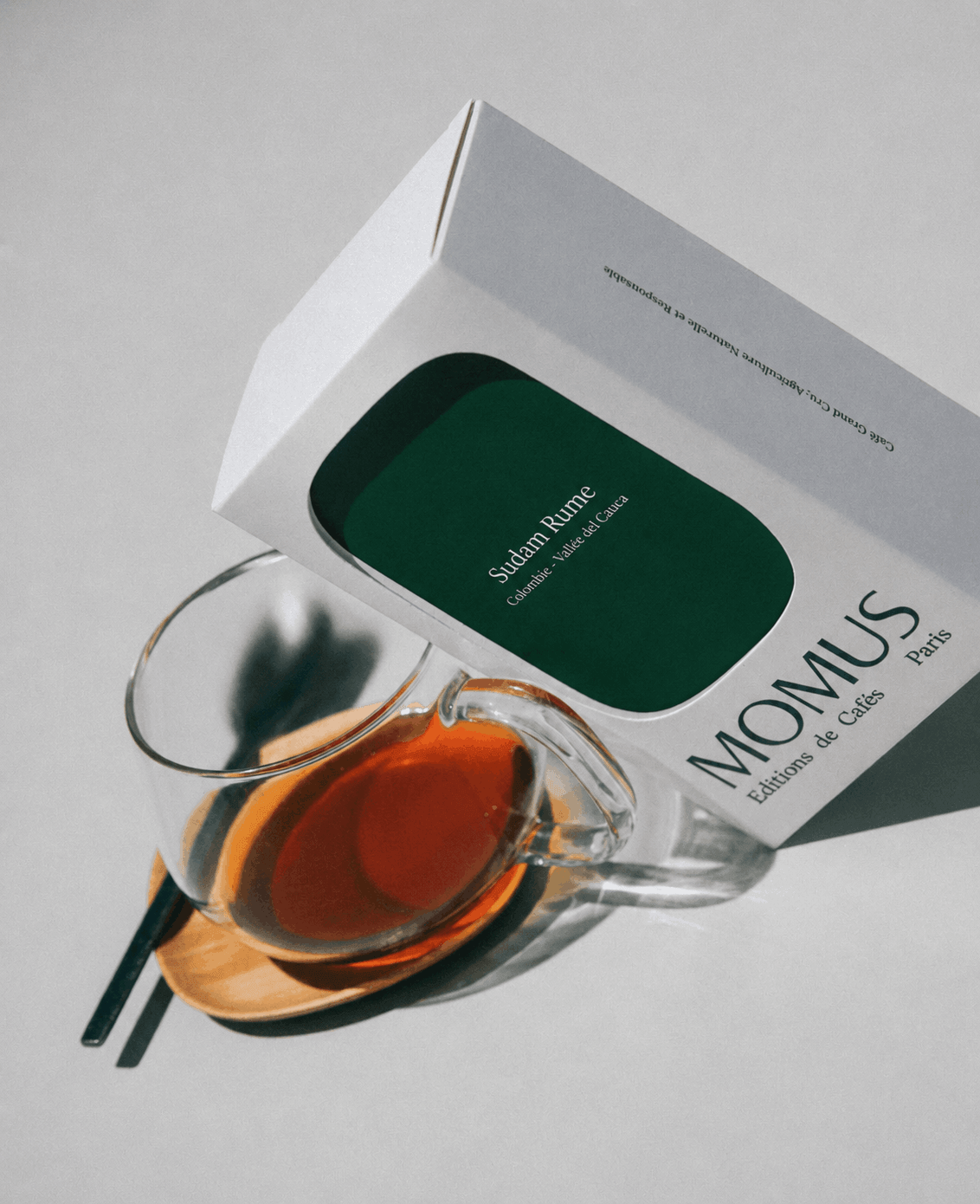 Café Sudam Rume présenté dans une tasse avec une boîte élégante, sur fond minimaliste.