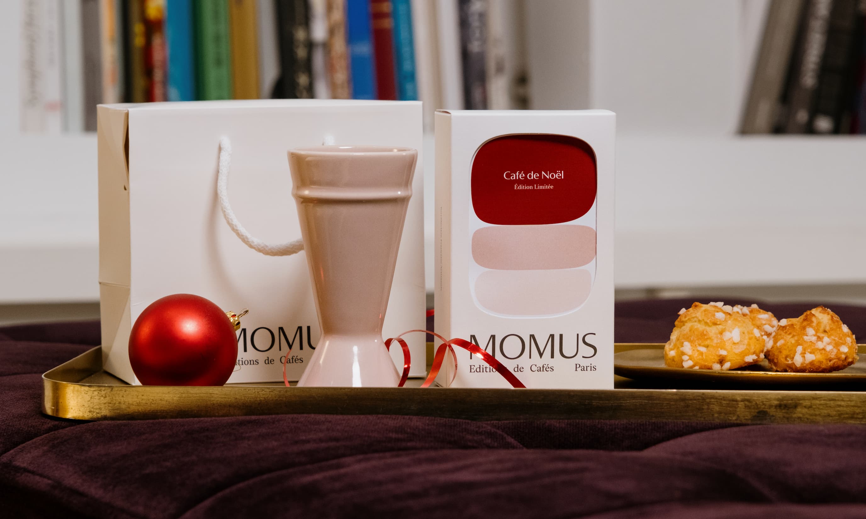 Coffret Café de Noël Momus avec tasse en céramique, boîte cadeau blanche, décoration de Noël rouge et petits choux sucrés, présenté sur un plateau doré.