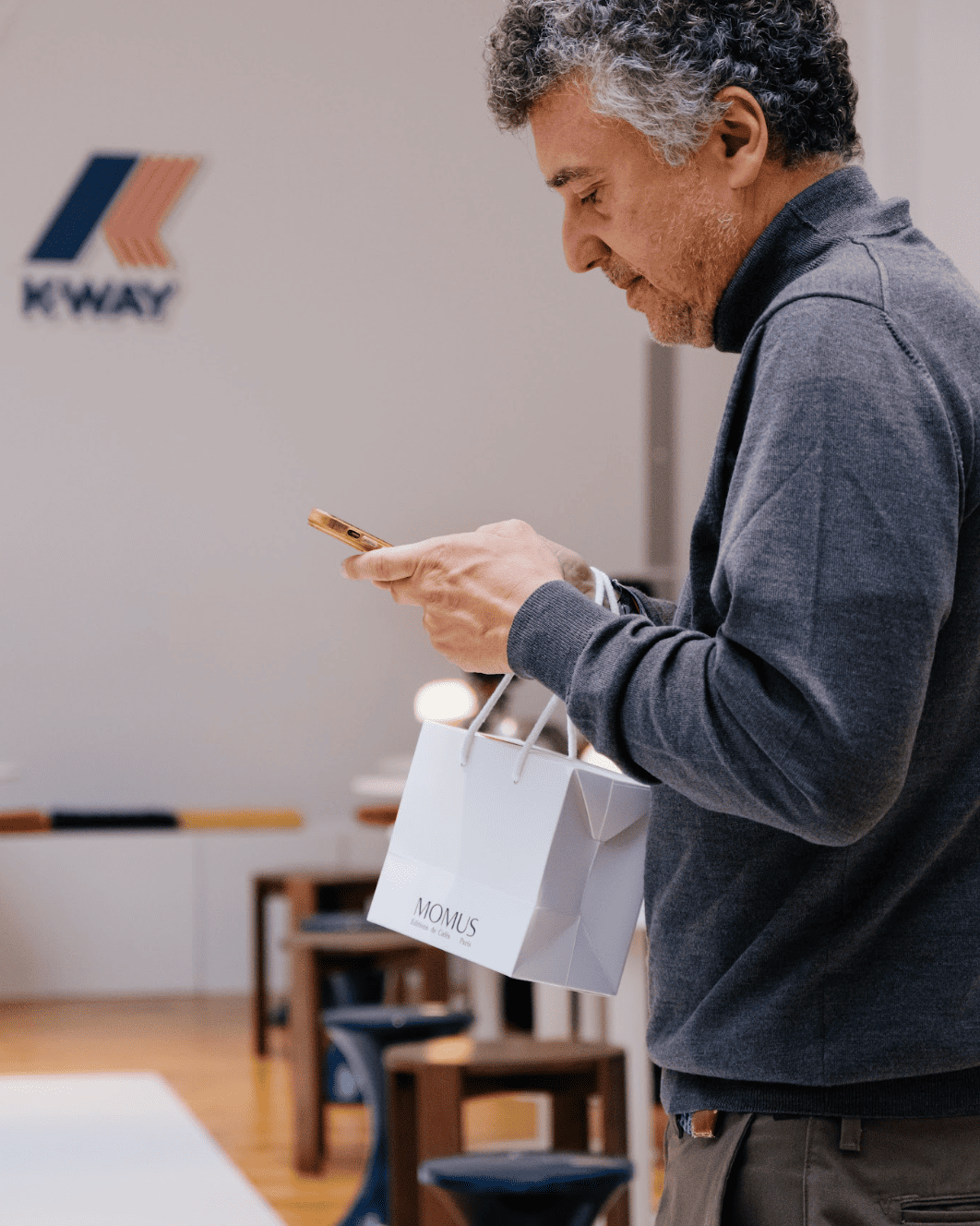 Un café avec Gianluisi Recuperati regardant son téléphone portant un sac cadeau Momus