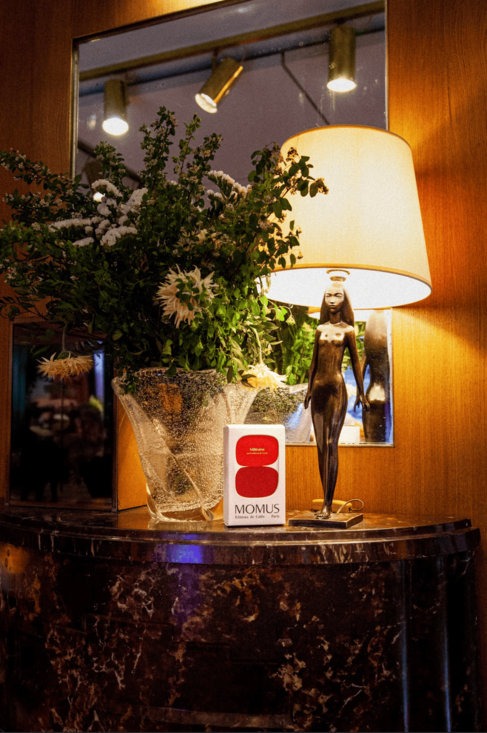Packaging Millésime Créé par Gwilerm de Cerval posé sur un table avec grand bouquet et lampe dont le pied est une femme en bronze