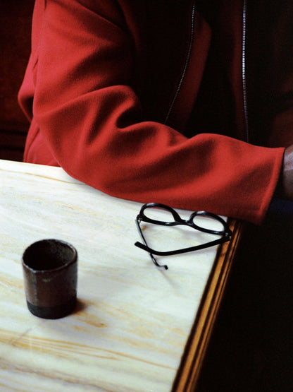 Avant bras de Stephane Abby posé. Veste rouge, lunettes noire sur la table et un café, Carbon. 