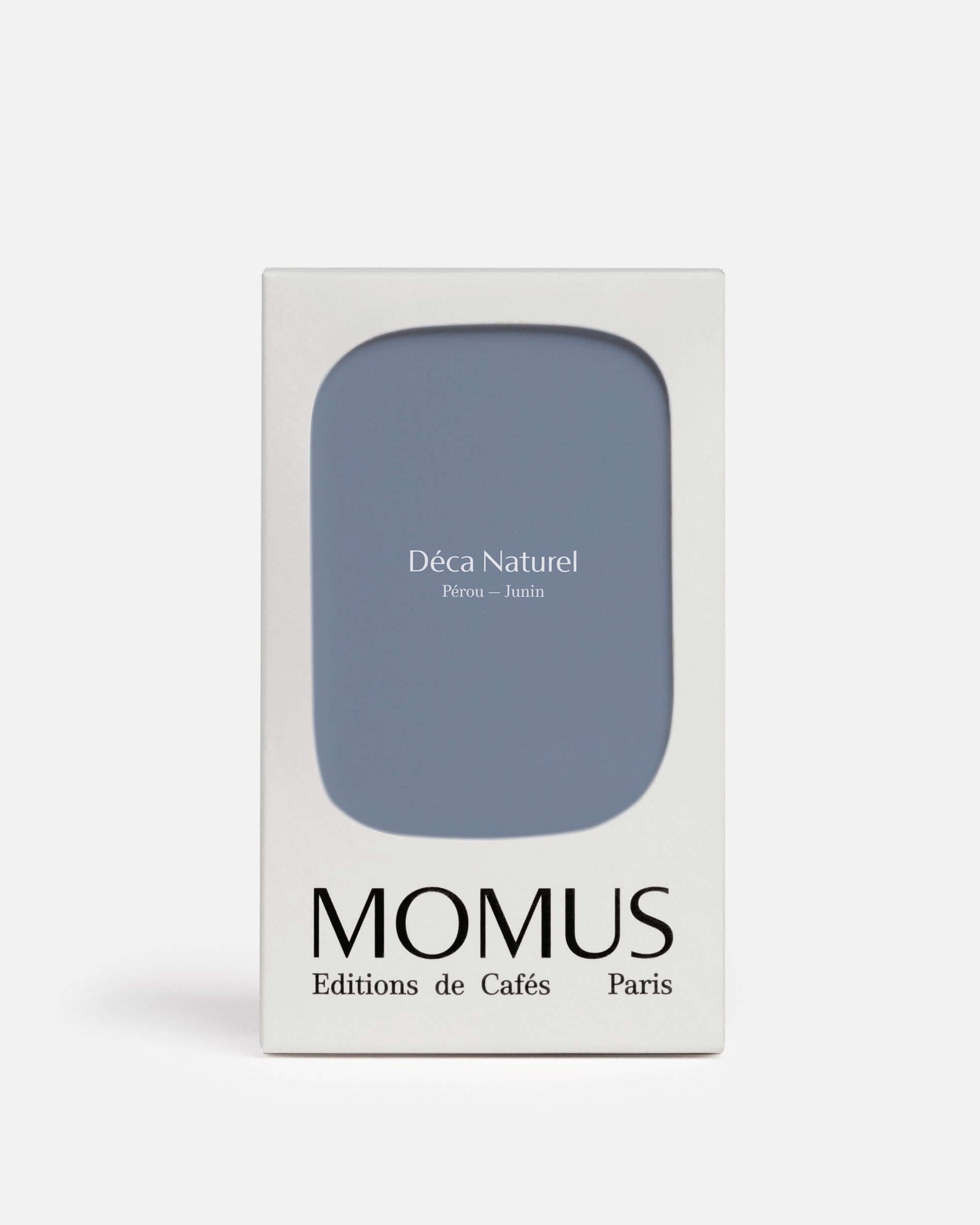 Packaging blanc du café Momus Déca Naturel Pérou – Junín. La boîte présente une grande forme bleu-gris clair. Ce café, décaféiné par le processus Swiss Water Bio, est issu d'Éthiopie Sidama (note : L'image indique Pérou-Junín mais le texte mentionne Éthiopie Sidama, j'ai inclus les deux pour le SEO). Cultivé par Haile Gebreselassié, il offre des notes de pêche, caramel et framboise tout en étant sans caféine et 100% arômes.