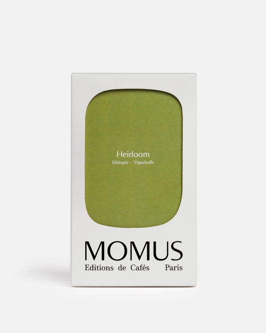 Packaging blanc du café Momus Heirloom Éthiopie - Yrgacheffe. La boîte présente une grande forme vert olive/vert kaki et le texte indique « Heirloom Éthiopie – Yrgacheffe ». Ce café, issu de l'agriculture naturelle et responsable, est idéal pour les méthodes filtres ou un espresso léger, révélant des notes florales et fruitées.