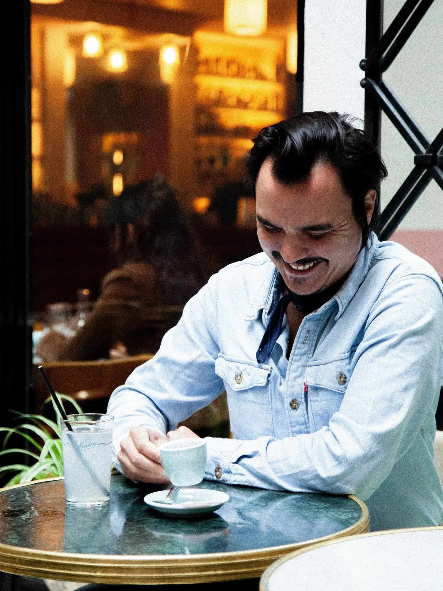 Portrait de Gwilherm de Cerval en chemise denim dégustant un espresso dans une ambiance bistrot. Le sommelier français collabore sur le Café Millésime - Biodynamie