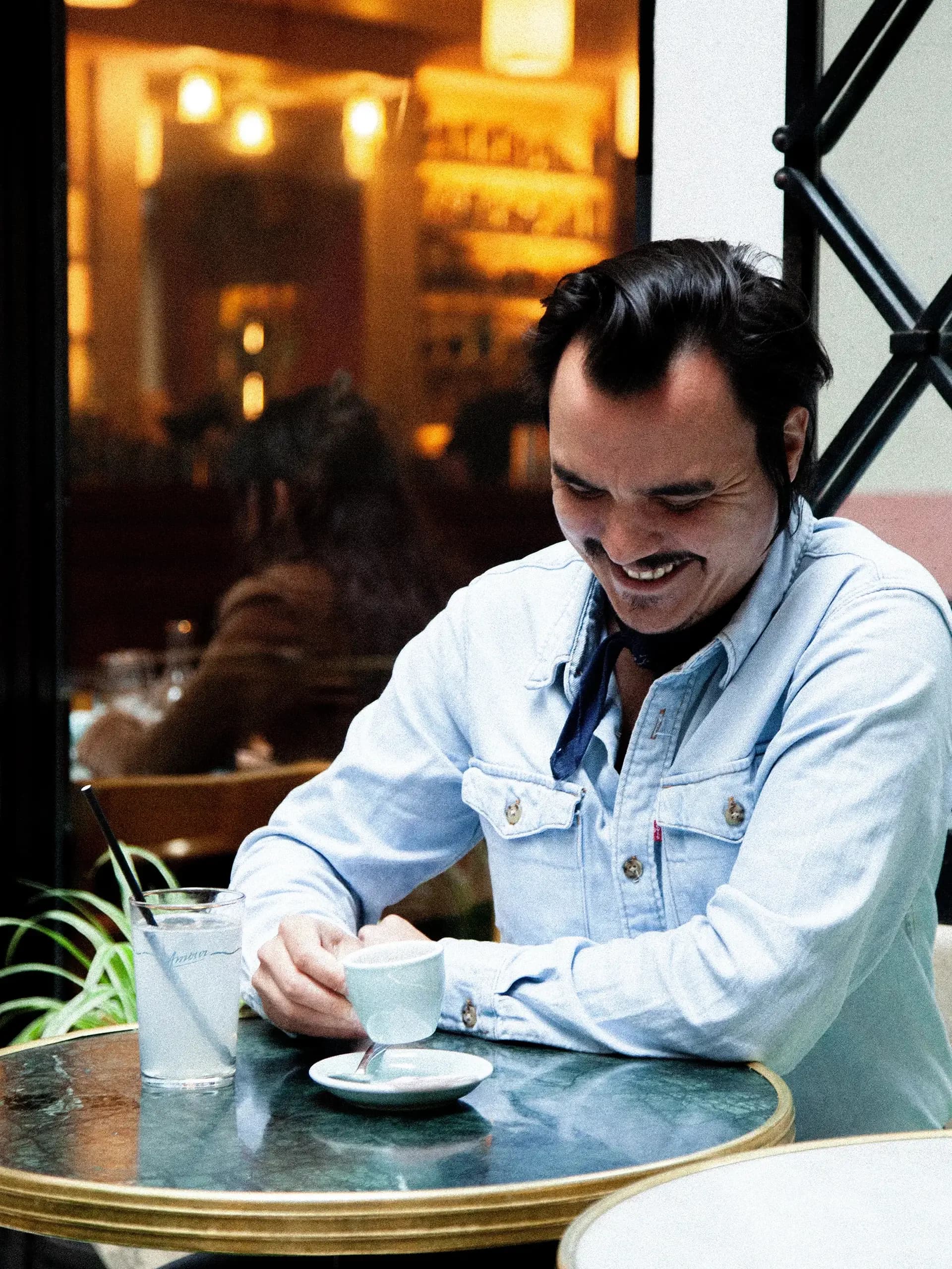 Portrait de Gwilherm de Cerval en chemise denim dégustant un espresso dans une ambiance bistrot. Le sommelier français collabore sur le Café Millésime - Biodynamie