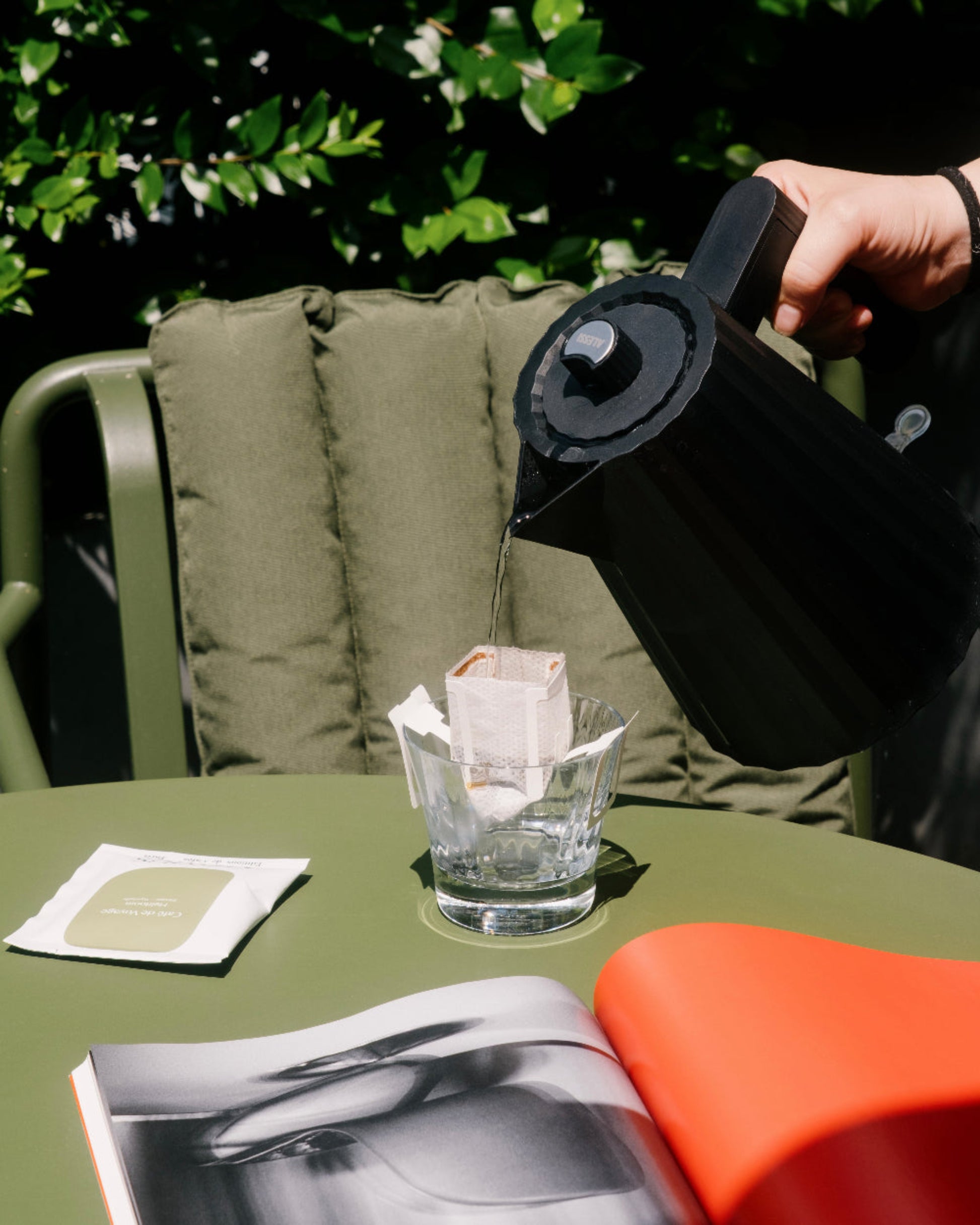 Eau chaude versée dans un sachet Drip Bag de café posé sur une table de jardin, pour savourer un café de spécialité où que vous soyez.