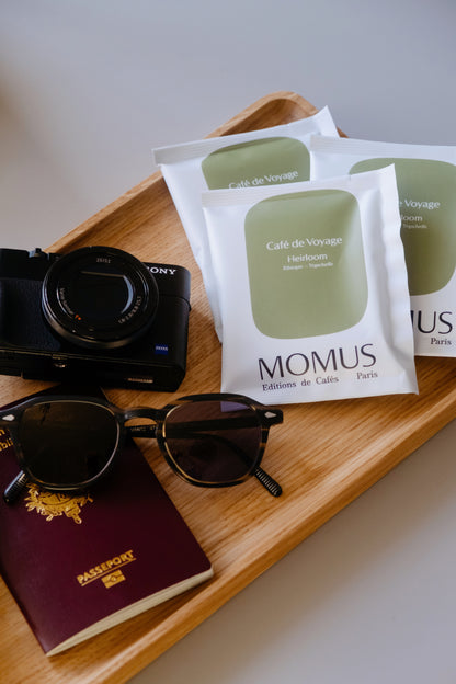 Plateau sur lequel est posé trois sachets Drip Bag avec à côté un petit appareil photo Sony, des Lunettes de soleil et un passeport; prêt pour les vacances