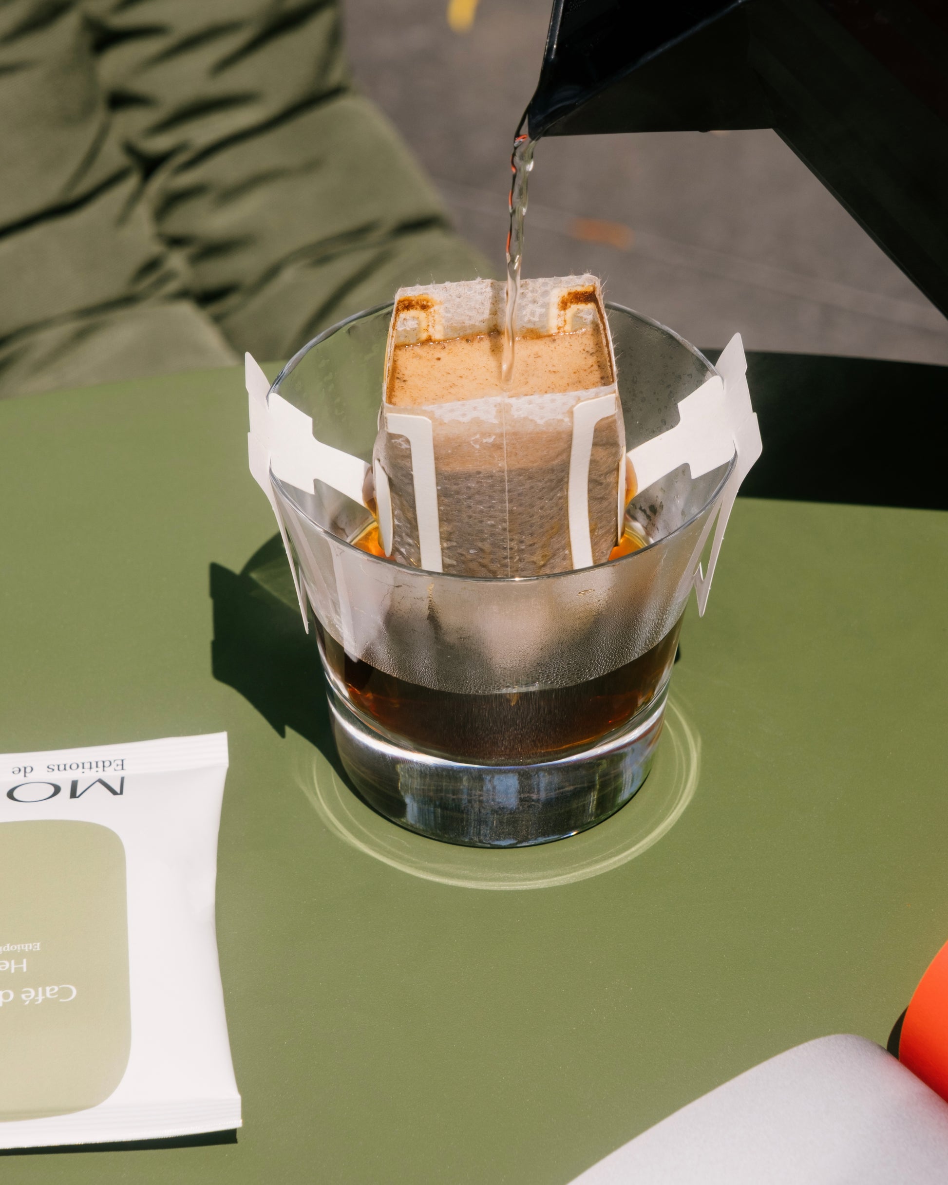 Plan rapproché : Eau chaude versée dans un sachet Drip Bag de café posé sur une table de jardin.