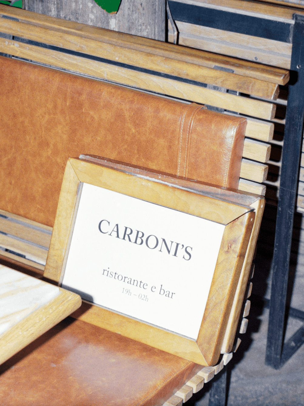 Enseigne du restaurant Carboni's de Stéphane abby posée sur une banquette en cuir dans un intérieur chaleureux en bois.