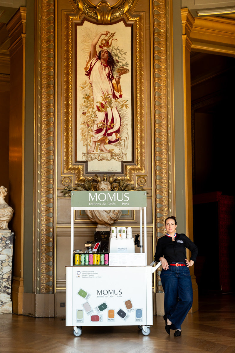 Un café à l'Opéra Garner - Daniela Capuano MOF accoudé à la charrette MOMUS, derrière elle un tableau représentant une femme qui sert du café