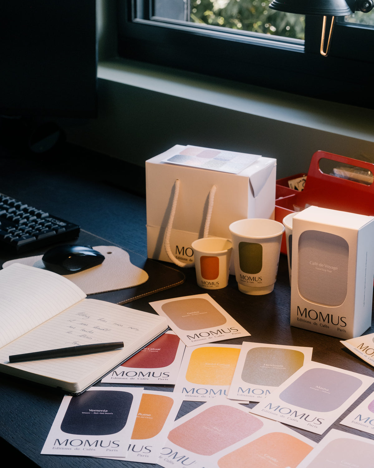 une table de travail avec les cartes cafés de la marque, les packaging et le sac Momus Paris Café de spécialité 